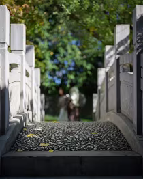 Between Permanence and Passage The stone bridge stands in sharp relief, its lines and textures seemingly unchanging. Beyond it, two figures dissolve into the softness of the background, their...