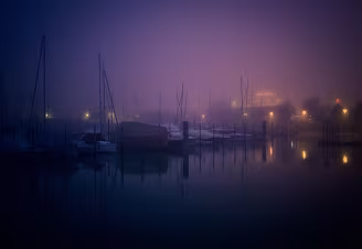 Between Stillness and Departure The boats rest silently beneath a veil of fog, their masts fading into shades of blue and violet. Distant lights glow softly through the mist, their reflections...